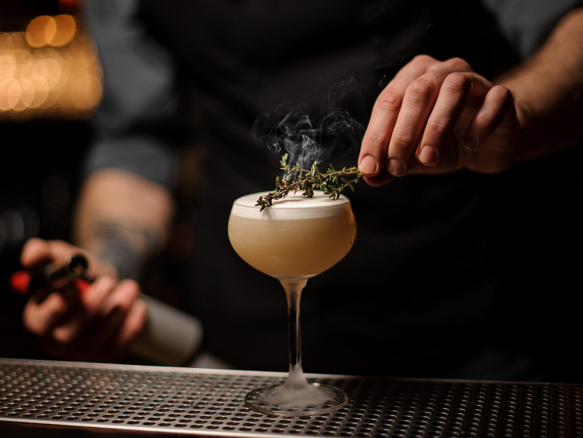 Bartender adds rosemary in alcohol light brown cocktail